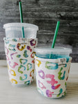 Rainbow Cheetah Iced Drink Snug. Tired of sweating iced drink cups?  Or ice just melting too fast in your cold drink?   Insulate your cup with a modern, stylish cup snug.  Keep your coffee cold, hands warm and water rings off the table.  It may also be used on hot cups.